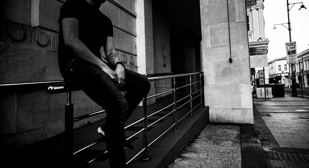 grayscale photo of person sitting on rail