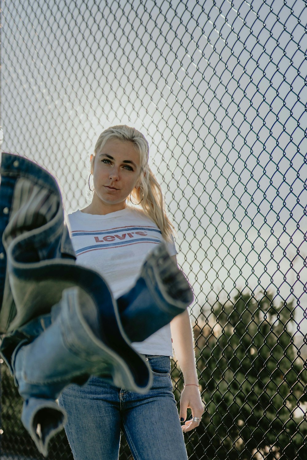 woman wearing blue jeans besides cyclone fence