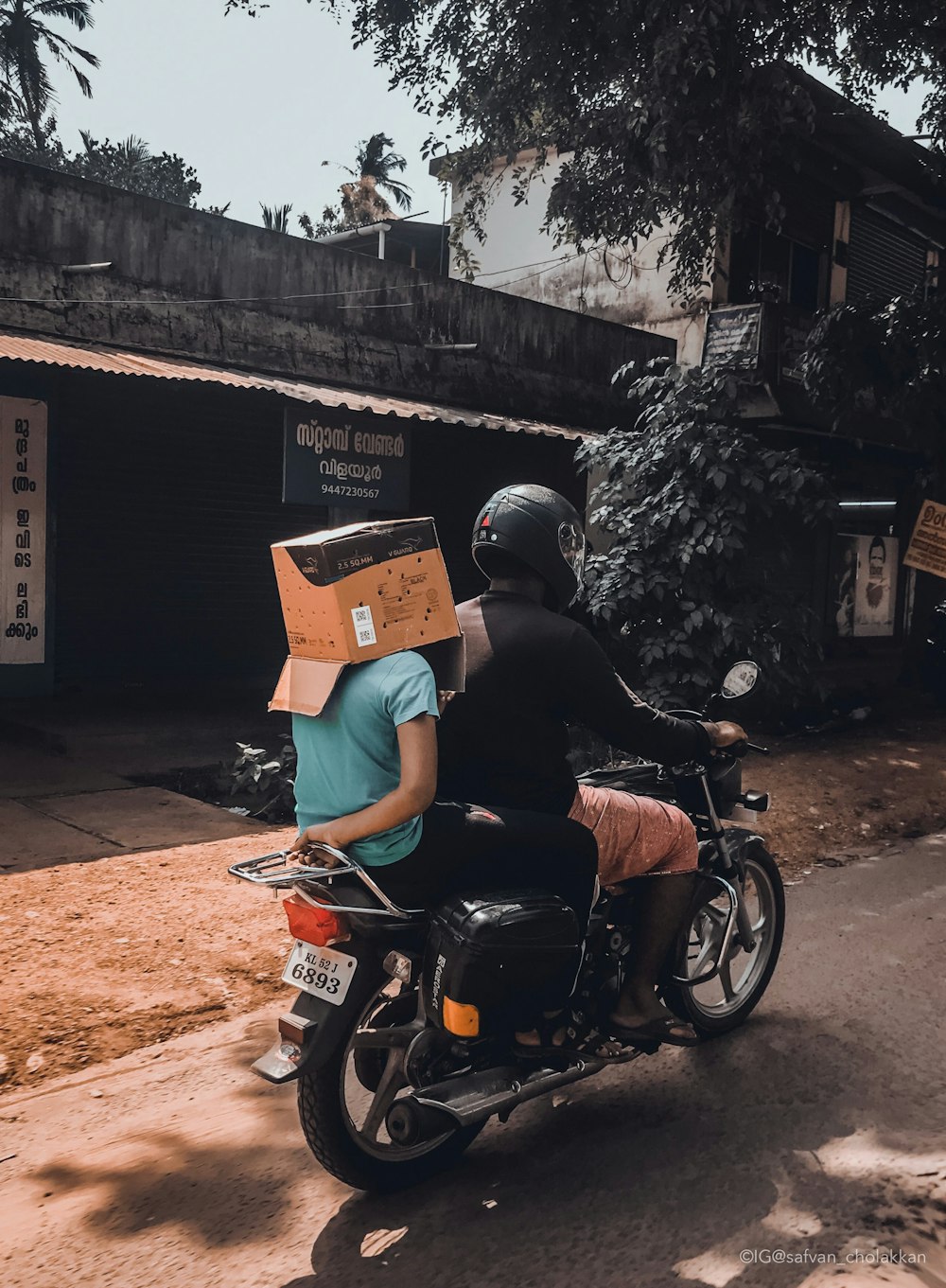 man riding motorcycle with person on his back with box on head