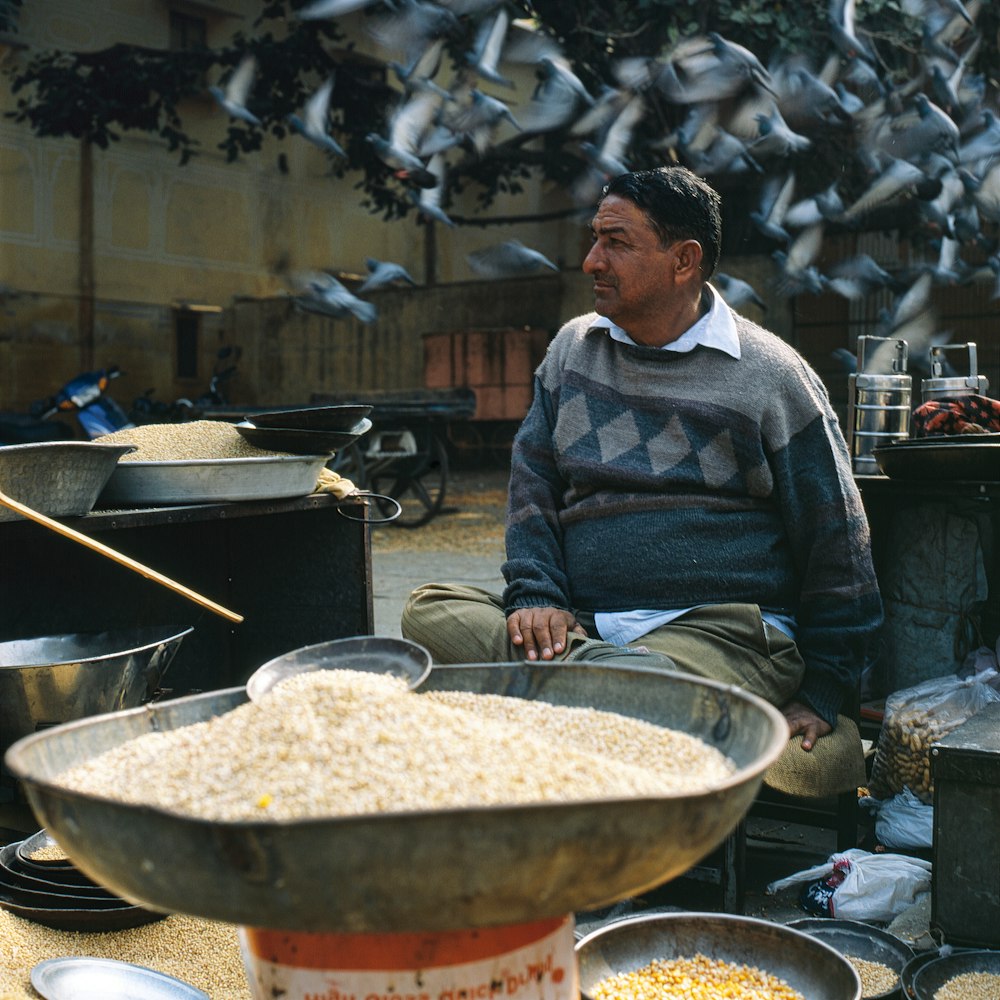 man in gray blue sweater sitting with birds flying behind