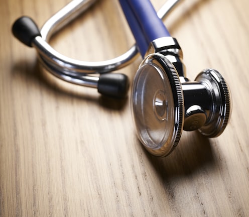 shallow focus photo of blue and gray stethoscope on brown wooden table