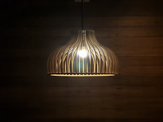 A warm Scandinavian wooden pendant light hanging over a rustic wooden table.