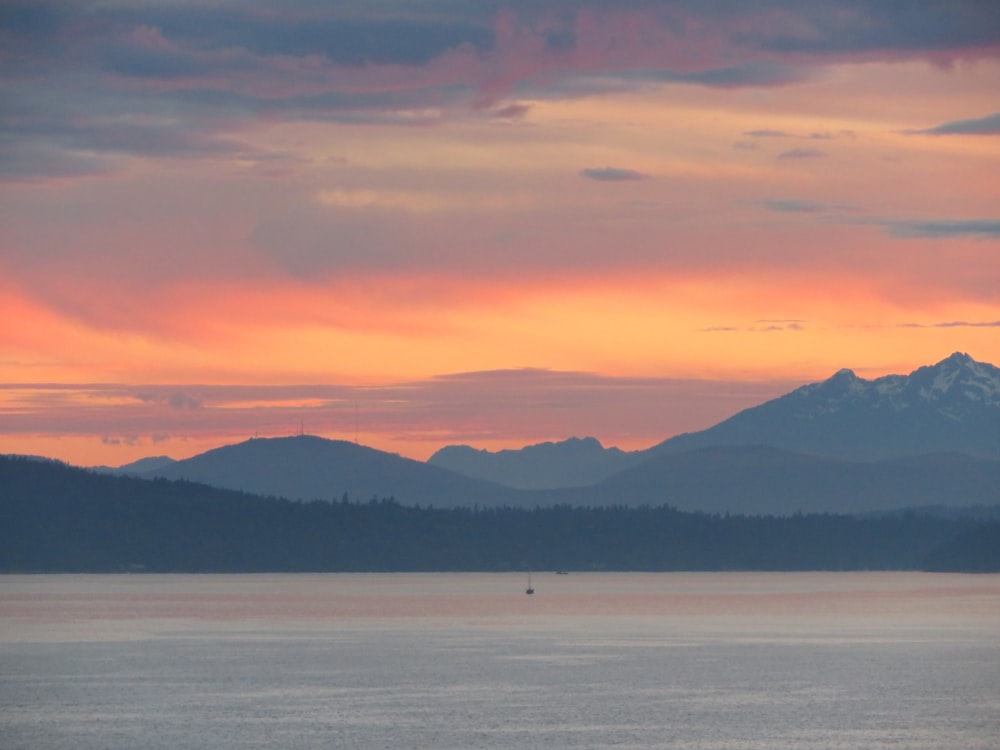 silhouette of mountains near body of water under cloudy sky during daytime