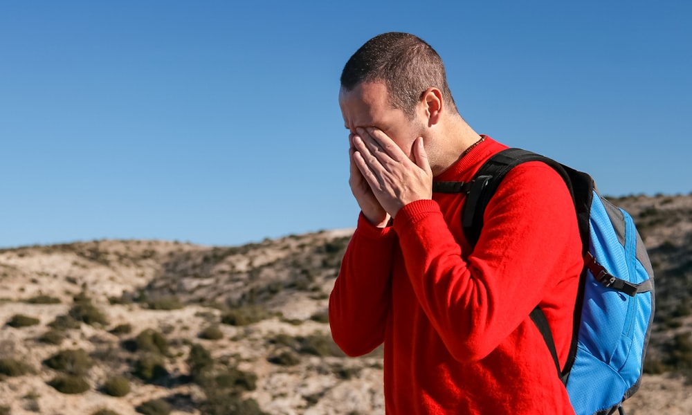 Mann trägt roten Pullover mit Rundhalsausschnitt und blaugrünem und schwarzem Rucksack im Freien während des Tages