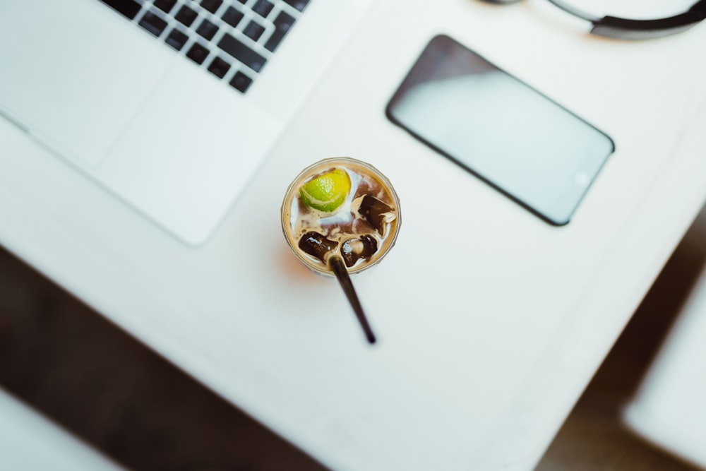 glass with food beside iPhone and laptop on table