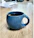 A close-up of a bright blue hand-thrown ceramic mug filled with steaming tea on a wooden table.