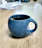 A close-up of a bright blue hand-thrown ceramic mug filled with steaming tea on a wooden table.