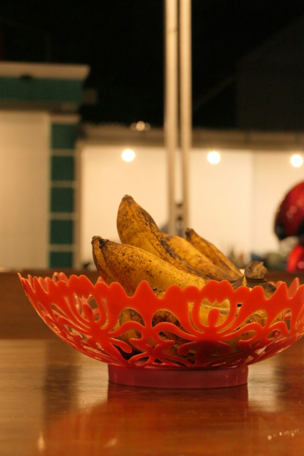 ripe banana fruits in red plastic bowl on table