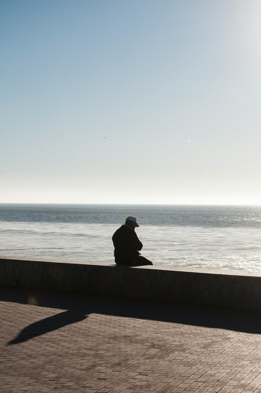 silhouette of man sitting beside seashore during daytime