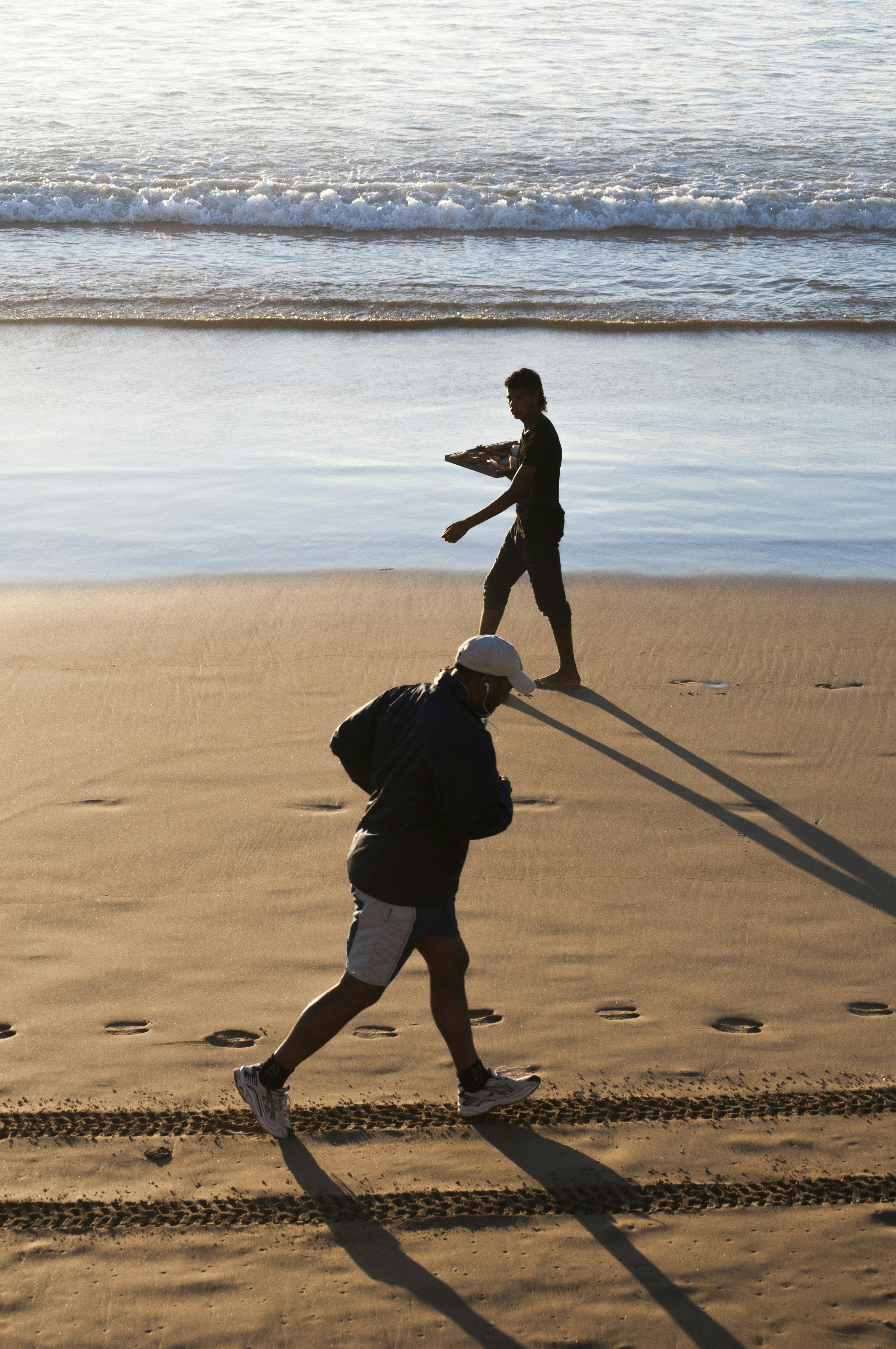 man walks with tray of food and man jogs at the beach