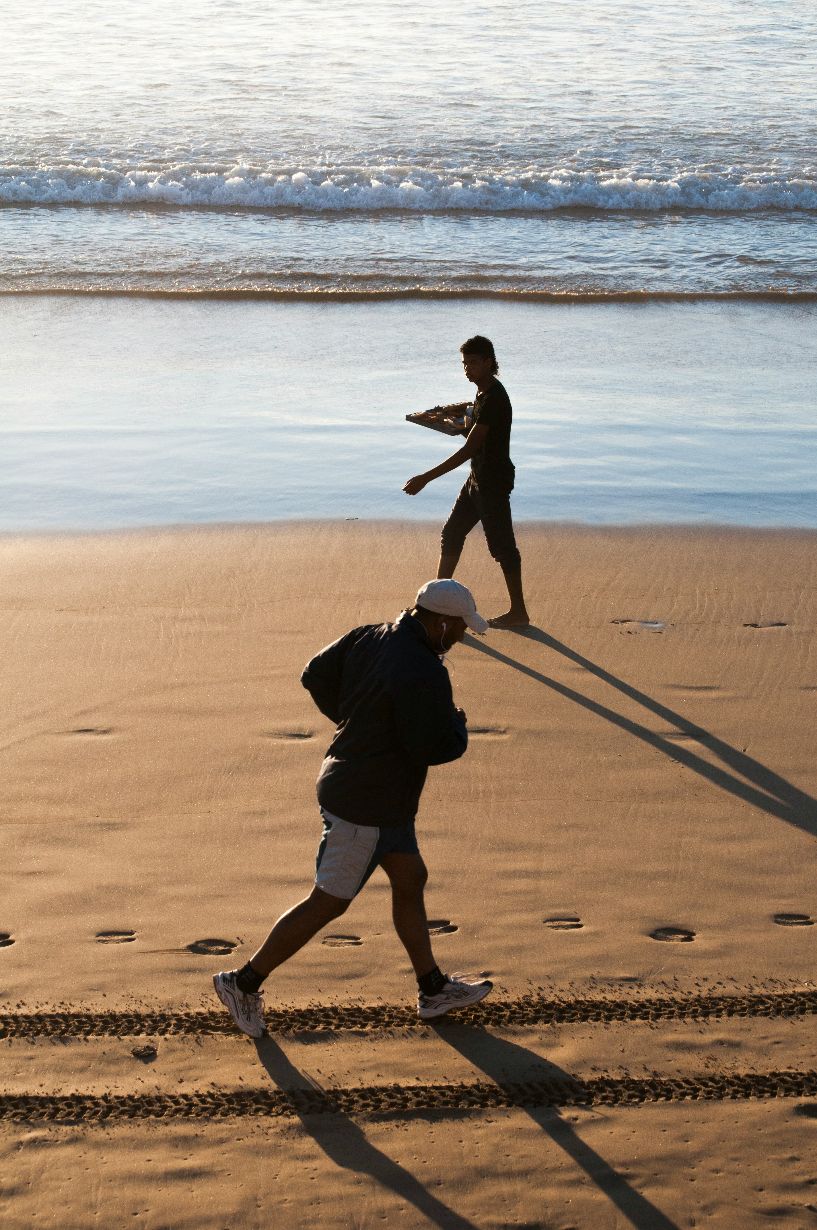 man walks with tray of food and man jogs at the beach