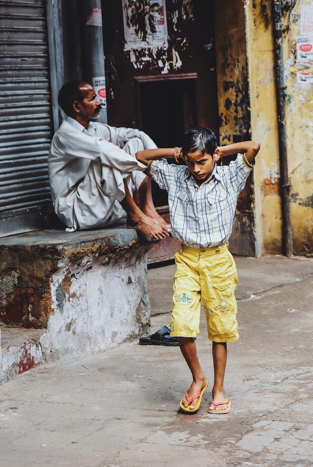 boy walking in front of man sitting beside roller shutter