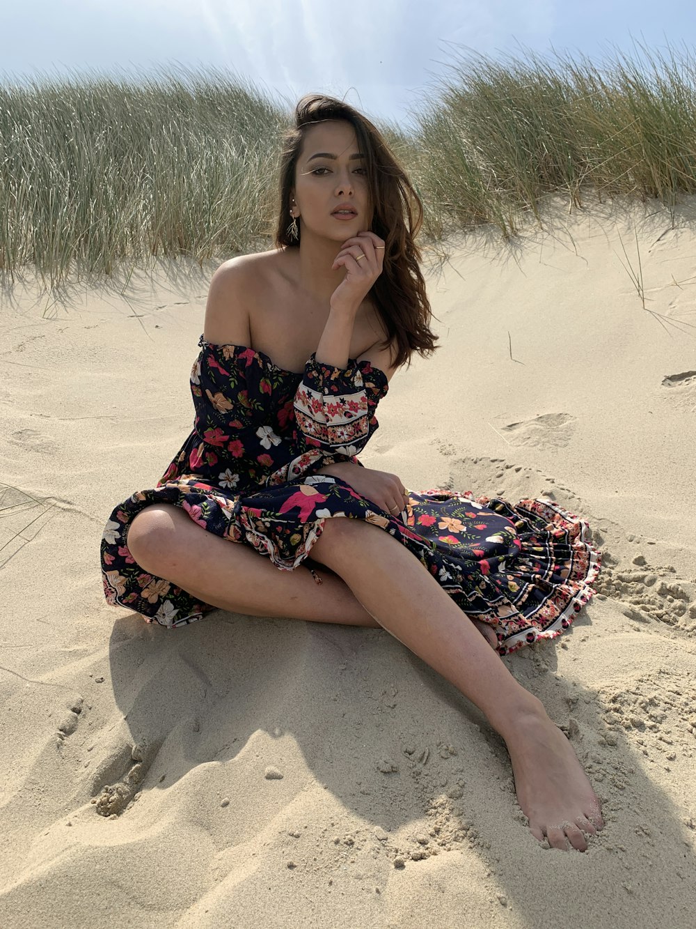 woman in black, pink, and white floral dress sitting on sand