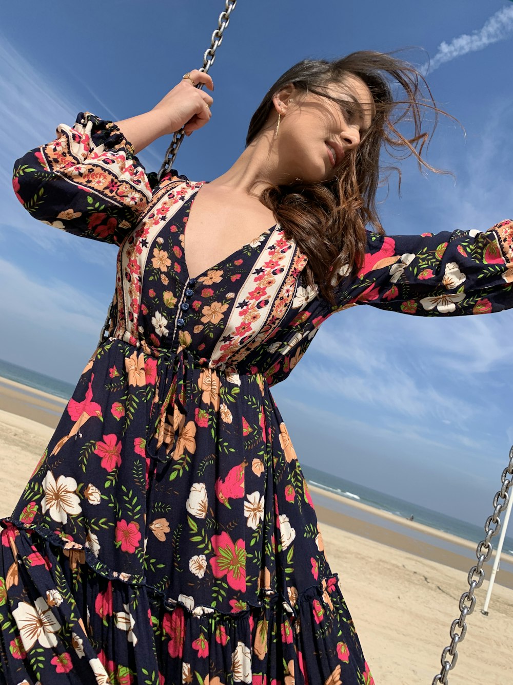 Femme portant une robe longue à fleurs bleues et multicolores tout en se balançant près de la plage