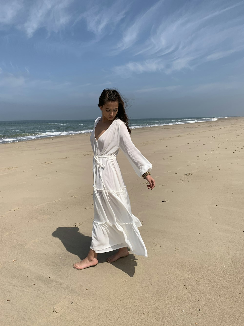 woman wearing long-sleeved dress walking on seashore