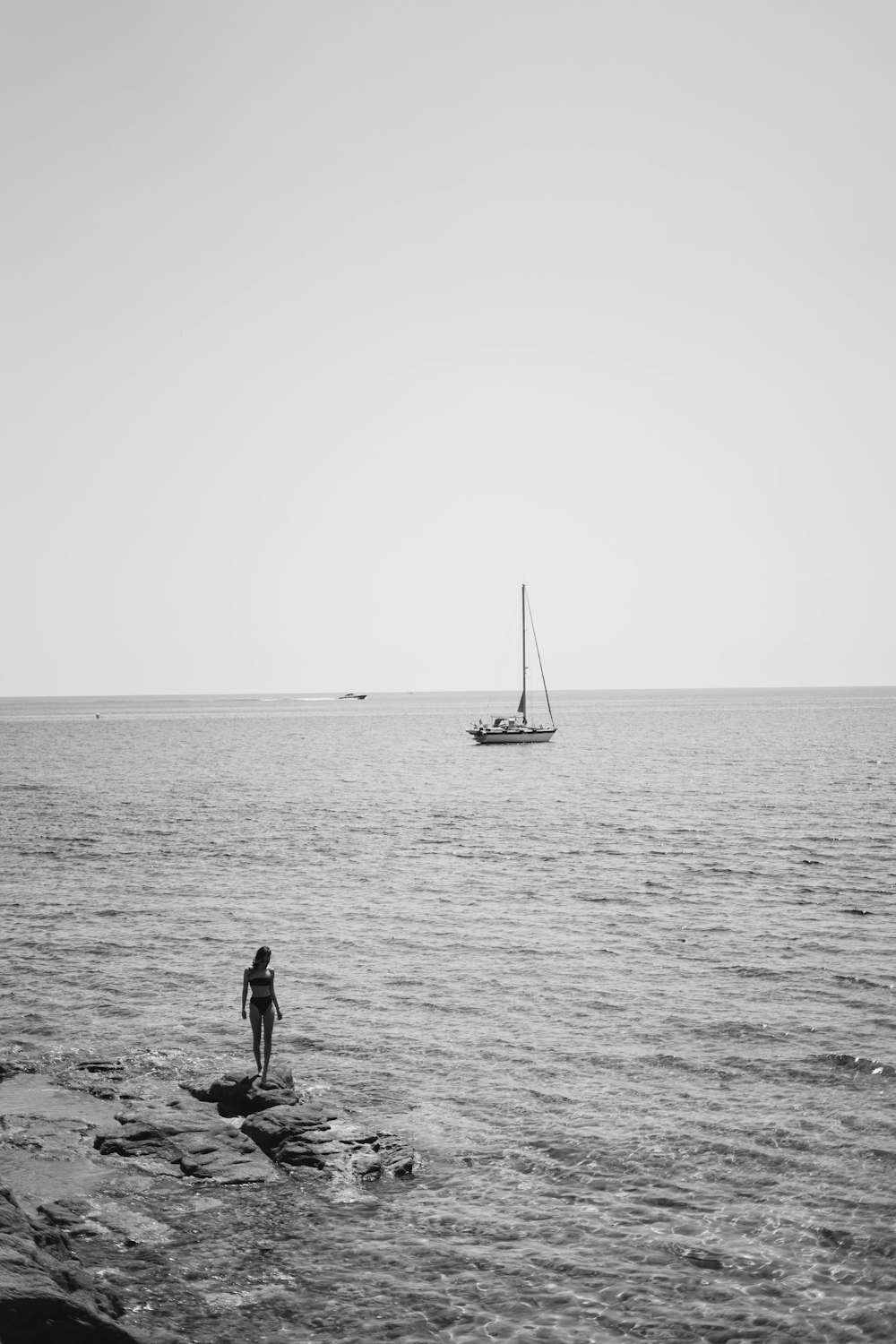woman in bikini standing on rock near sailboat