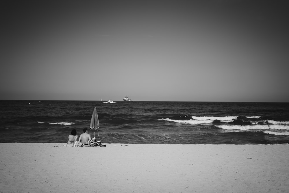 grayscale photo of boy and girl sitting on shore