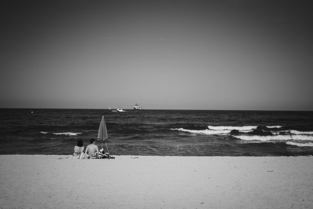 Photo en niveaux de gris d’un garçon et d’une fille assis sur le rivage