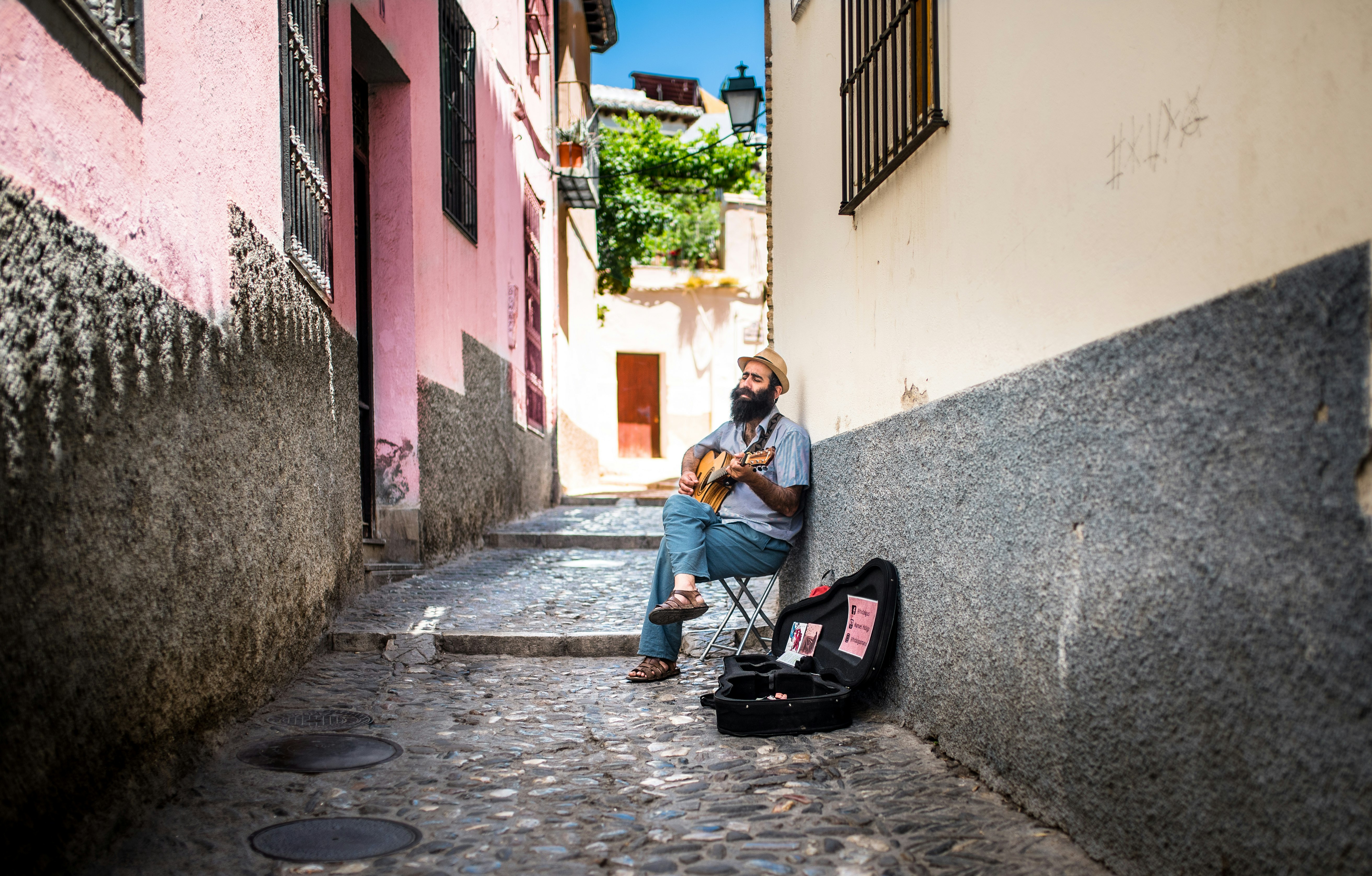 sitting man playing guitar with open guitar bag on side on allway