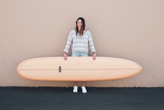 woman wearing gray and white stripe long-sleeved shirt holding brown surfboard