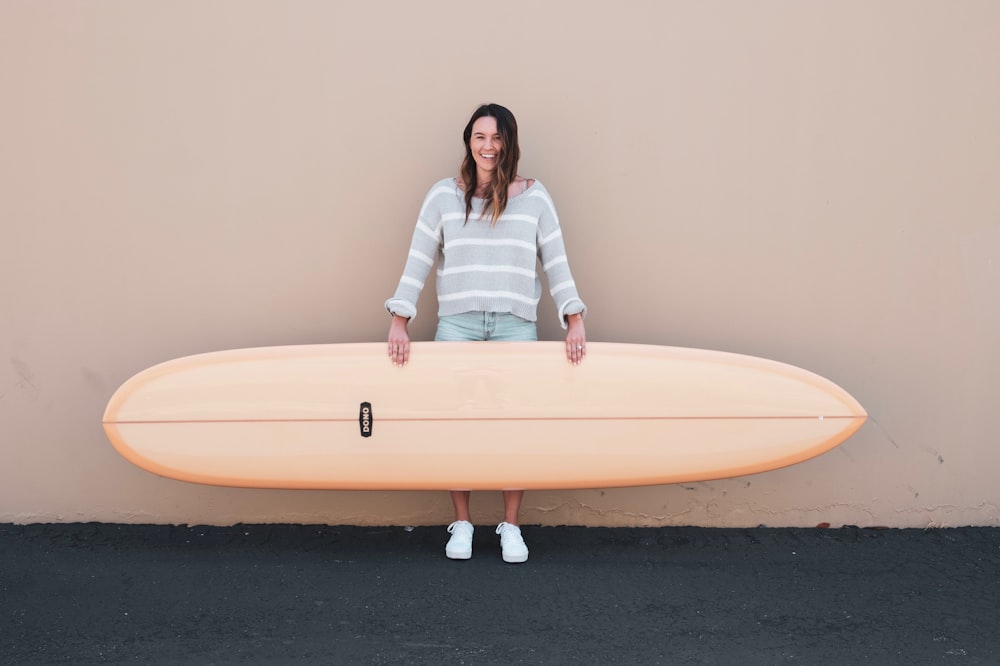 Donna che indossa una camicia a maniche lunghe a strisce grigie e bianche che tiene una tavola da surf marrone