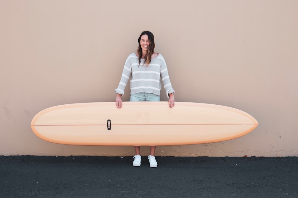 woman wearing gray and white stripe long-sleeved shirt holding brown surfboard