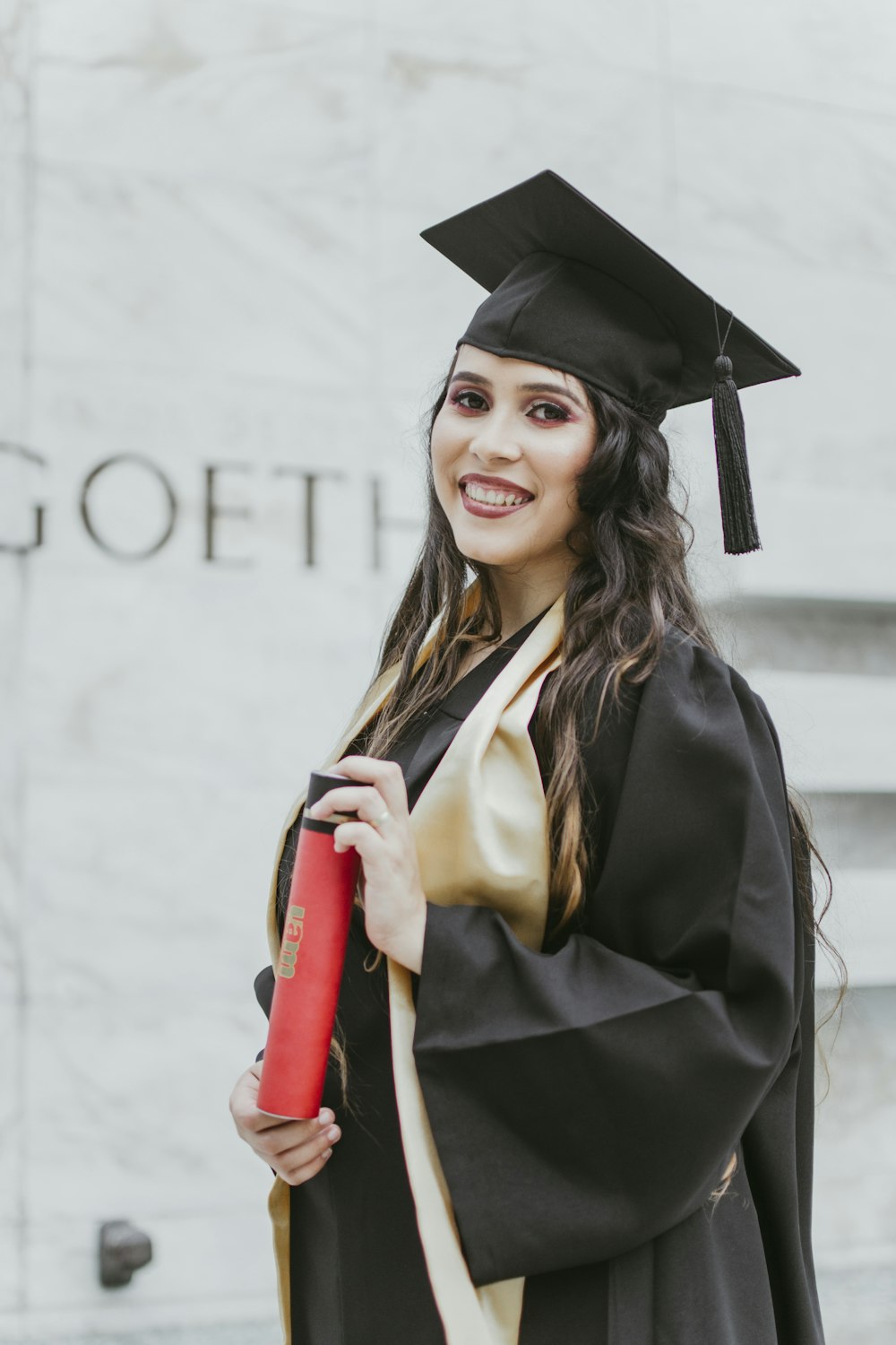 smiling woman in academic gown standing near wall