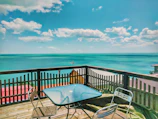 Guests laughing and relaxing on a wooden deck overlooking turquoise waters under a clear blue sky.