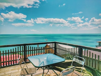 Minimalist wooden deck overlooking a calm turquoise bay with a single hibiscus flower on the railing.
