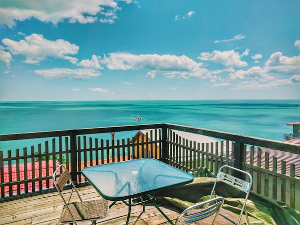 Minimalist wooden deck overlooking a calm turquoise bay with a single hibiscus flower on the railing.