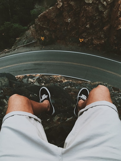 man sitting on cliff near road
