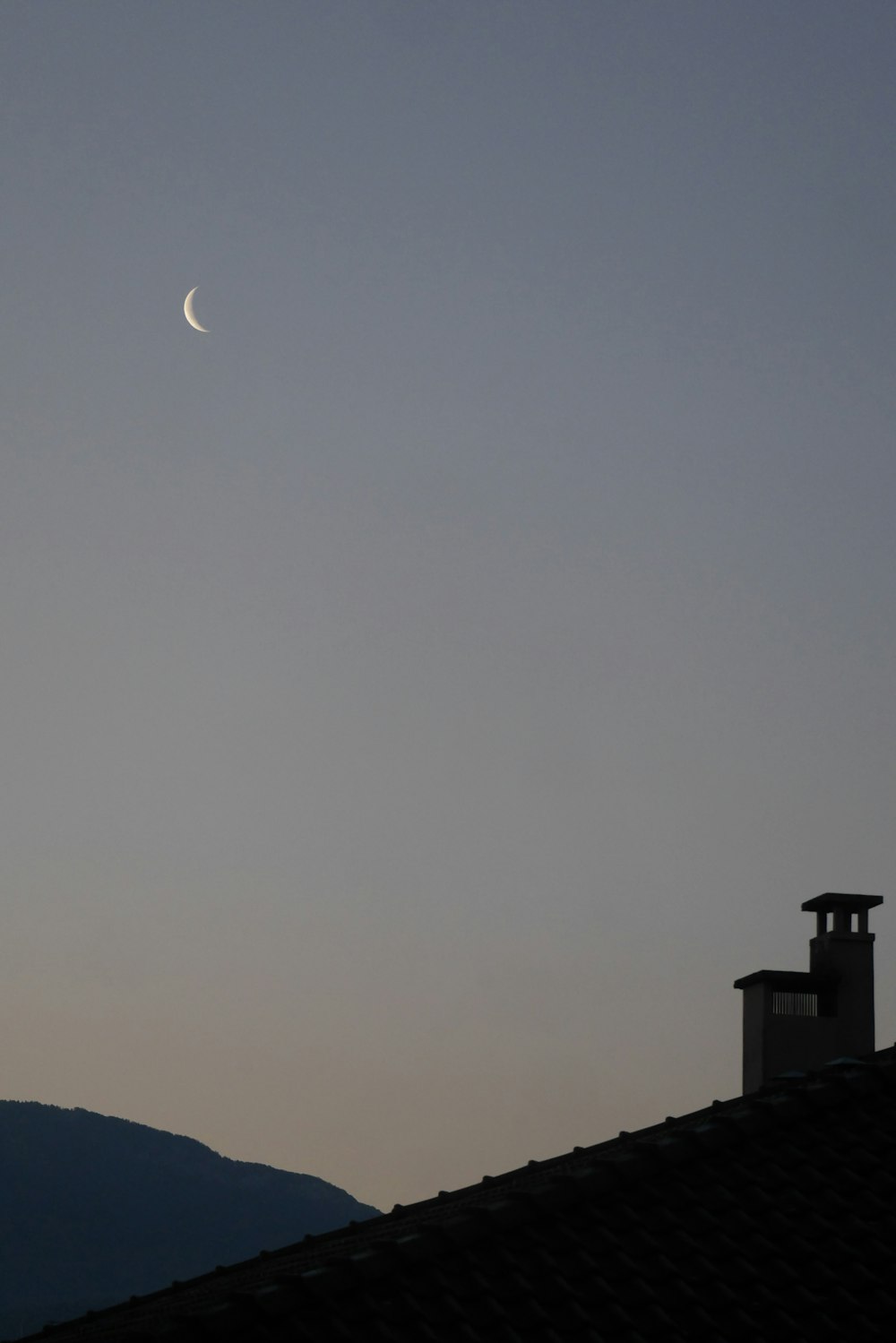 the moon is seen in the sky over a roof