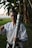 A person wearing a martial arts uniform holds a decorated torch with a firm grip, standing in a grassy outdoor setting surrounded by trees. The individual has a determined expression and is making a fist with their other hand.