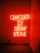 Bright neon text illuminates a dimly lit space, casting a warm orange glow on the surrounding walls. The message conveys a sense of comfort and acceptance.