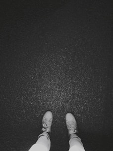 Two feet are visible in light-colored sneakers standing on a dark, textured surface, possibly asphalt.