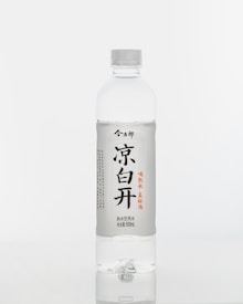 A clear plastic bottle filled with water, featuring a white label with black and red text and Asian characters. The bottle has a white cap and a simple, minimalist design, placed against a white background.