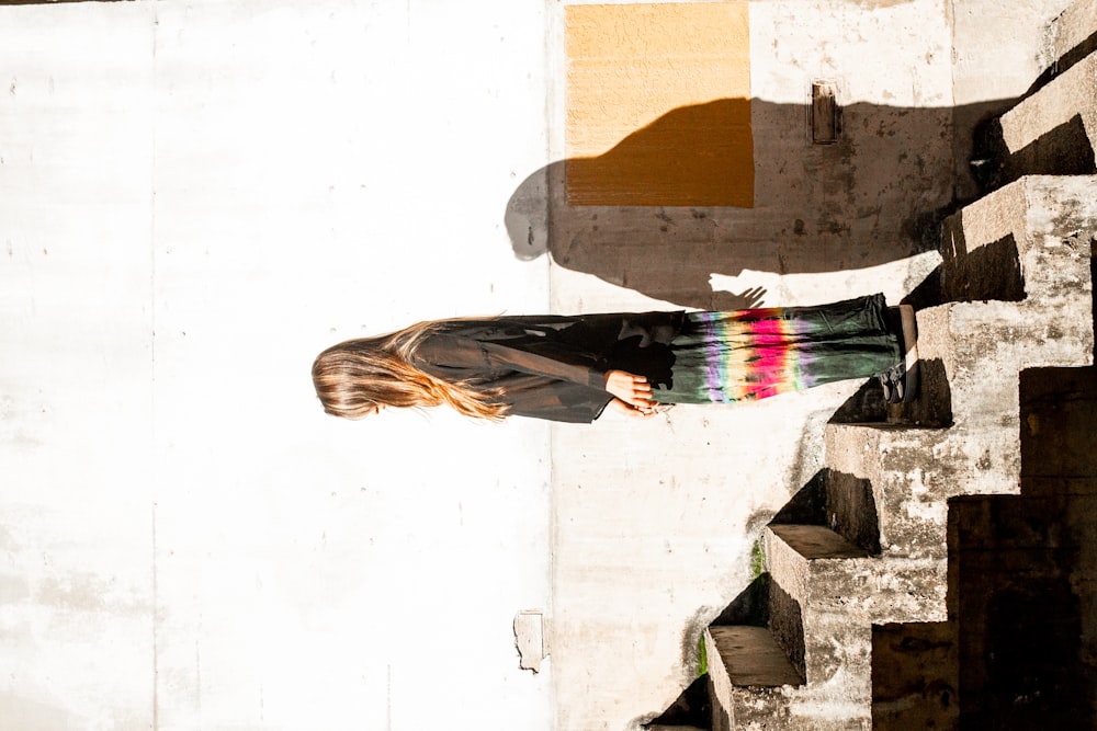 Femme en chemise noire à manches longues et jupe multicolore debout sur les escaliers