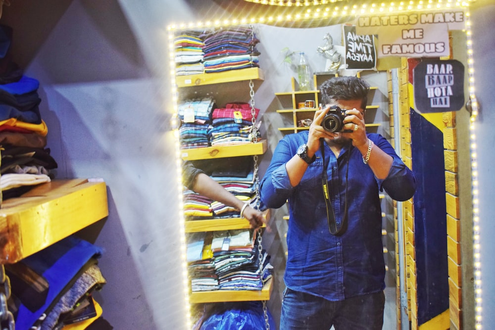 man in blue dress shirt taking picture with black DSLR camera