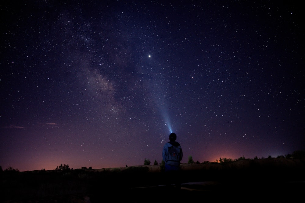 a man standing on a hill looking up at the night sky