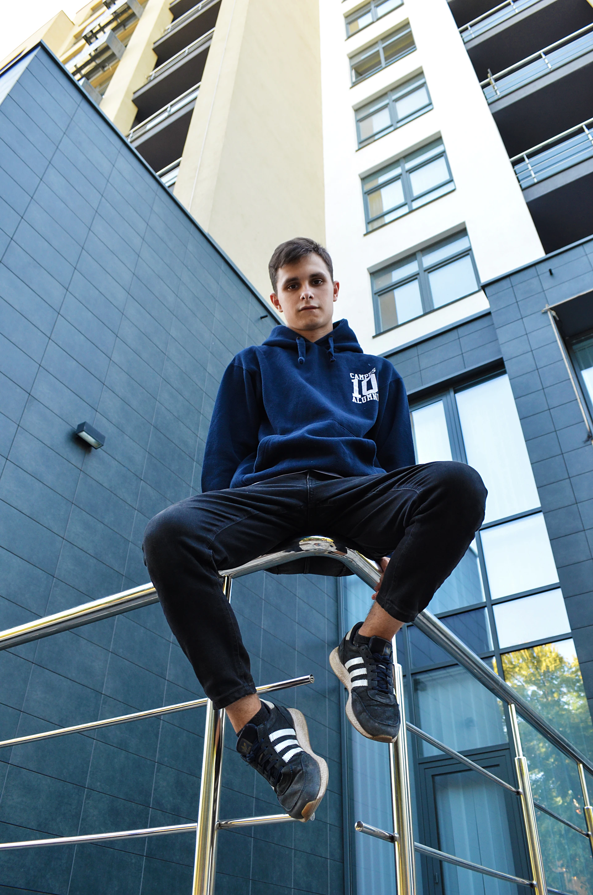 man wearing blue pullover hoodie sitting on fence