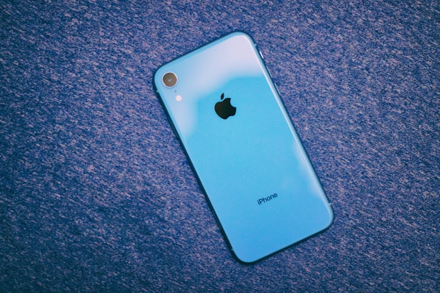 A blue iPhone with the Apple logo placed on a textured blue surface. The phone is positioned at an angle, showcasing the back design.