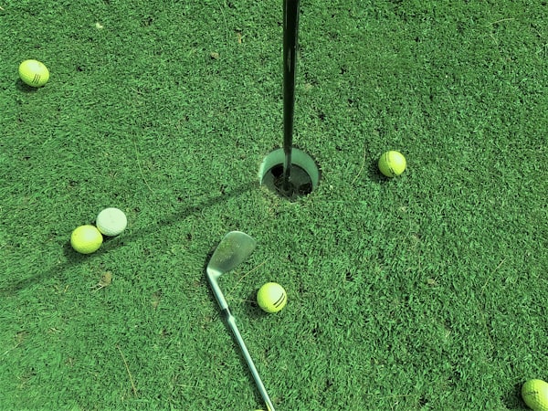 six golf balls near hole and one golf club