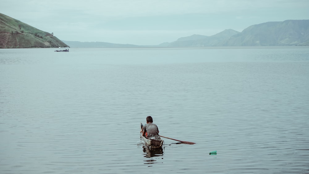 person sitting on brown boat viewing mountain during daytime