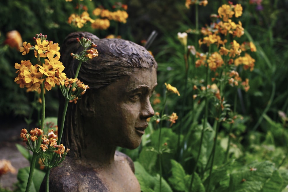 woman head statue in between blooming yellow flowers