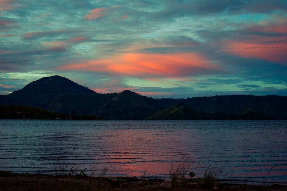 blue calm sea viewing mountain under green and orange skies