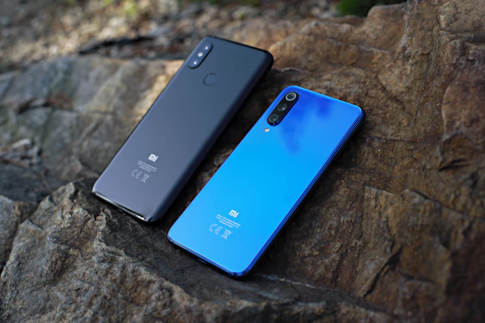 Two Xiaomi smartphones, one black and one blue, resting on rock