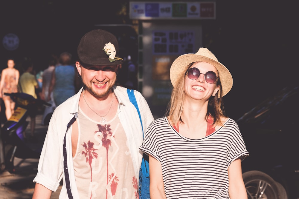 two smiling man and woman in front of people and car