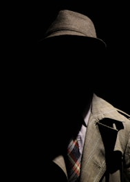 person wearing gray plaid notched lapel suit jacket and gray hat hiding face