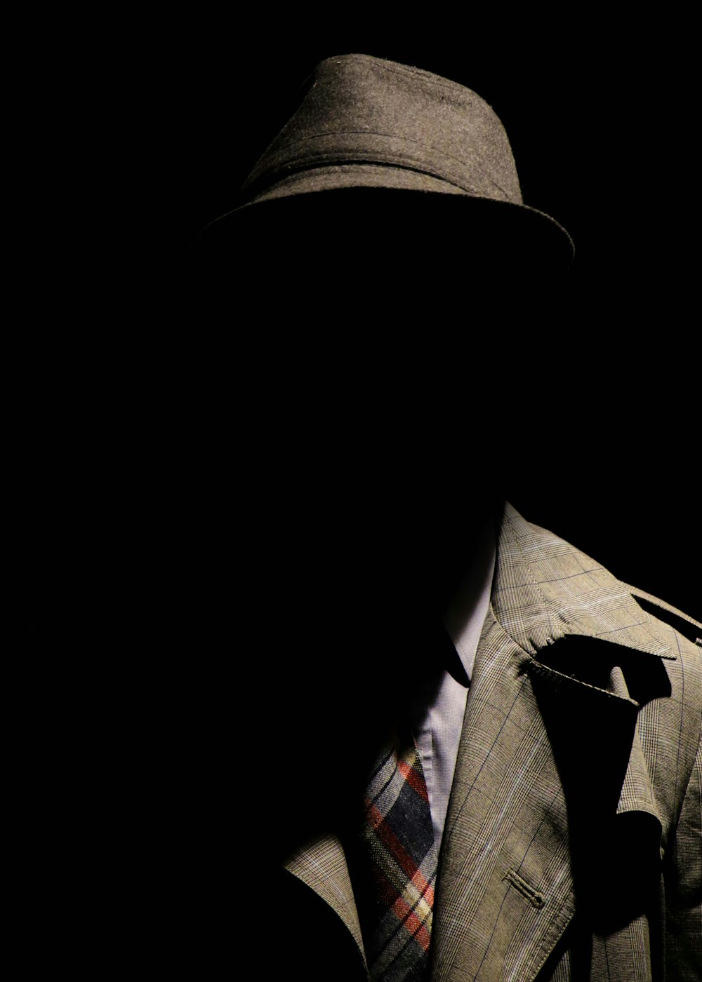 person wearing gray plaid notched lapel suit jacket and gray hat hiding face