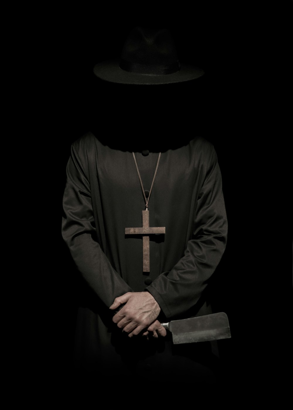 personne debout portant un chapeau et un collier de croix tenant un couperet